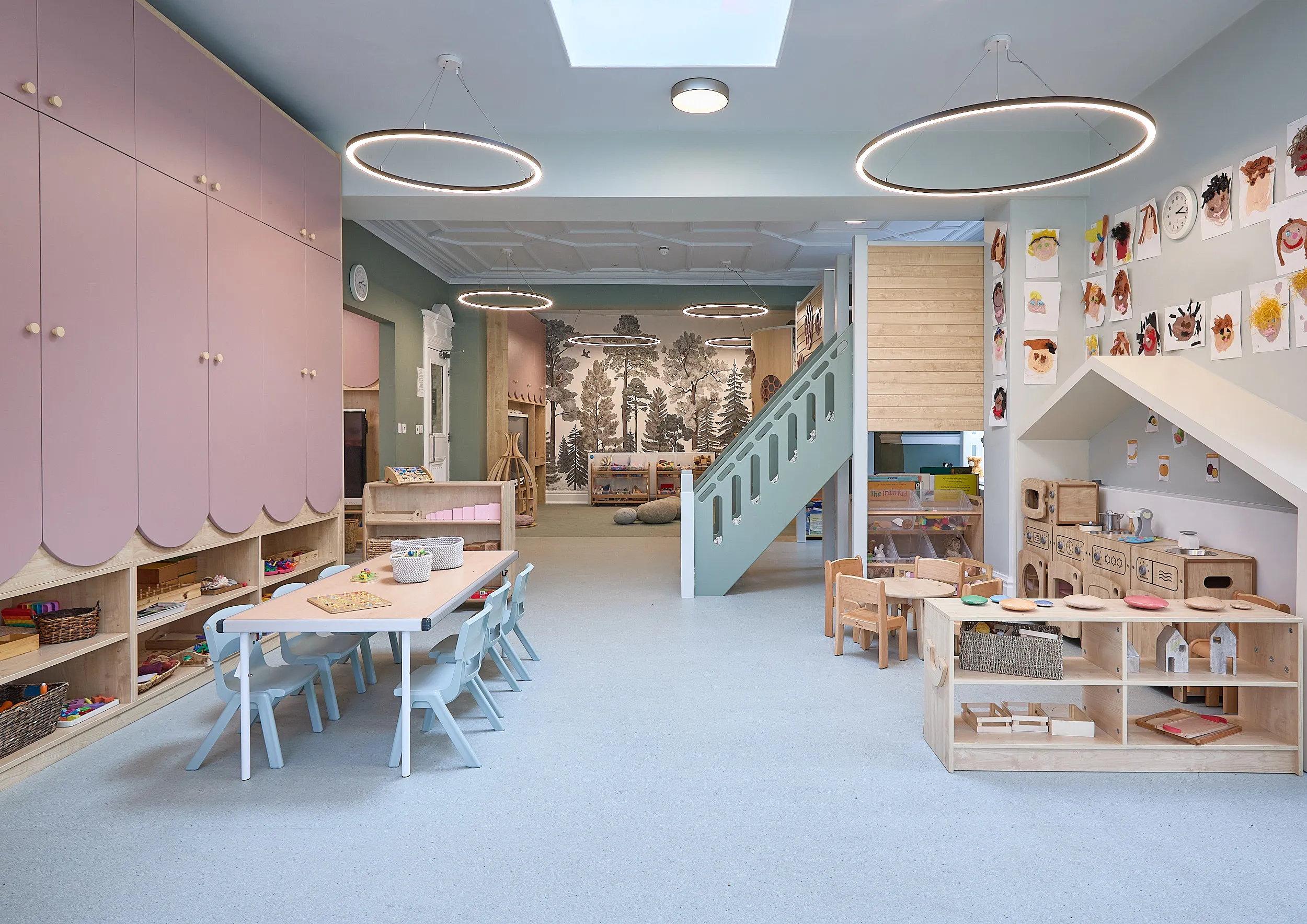 Pastel nursery playroom with pink joinery, mint staircase, ring pendant lights, and child-scaled wooden furniture